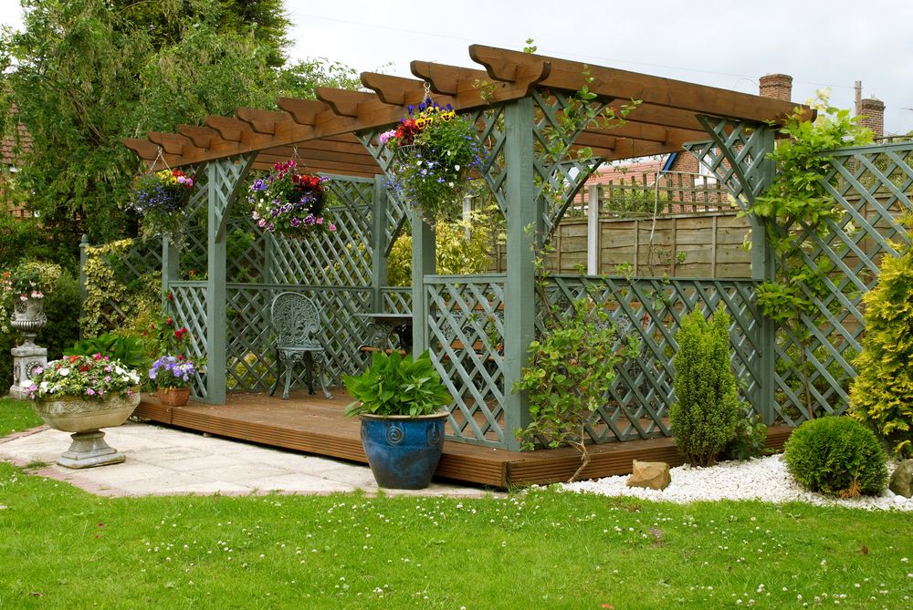 This is an image of a beautiful garden pergola with sitting area and table underneath.